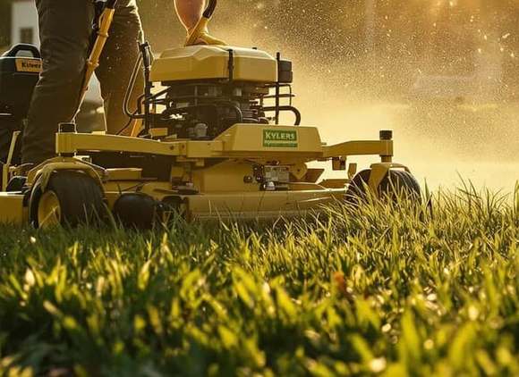 A yellow walk-behind mower deck cutting through thick green grass, clippings spraying into
golden backlight.